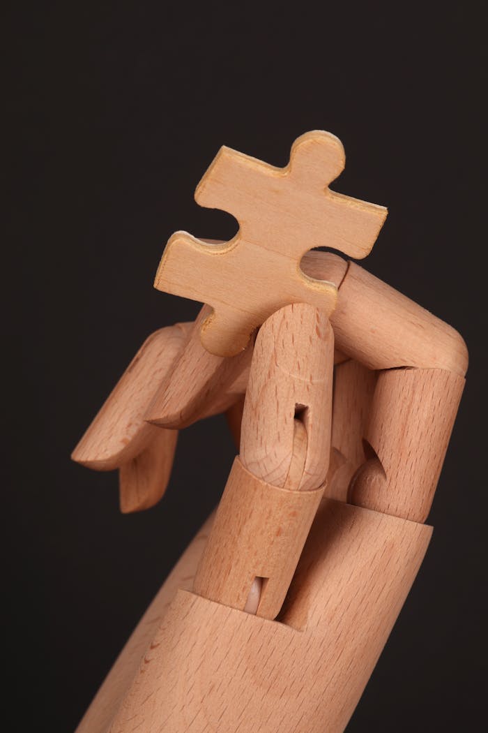 A wooden mannequin hand holding a jigsaw puzzle piece on a dark background, symbolizing problem-solving.